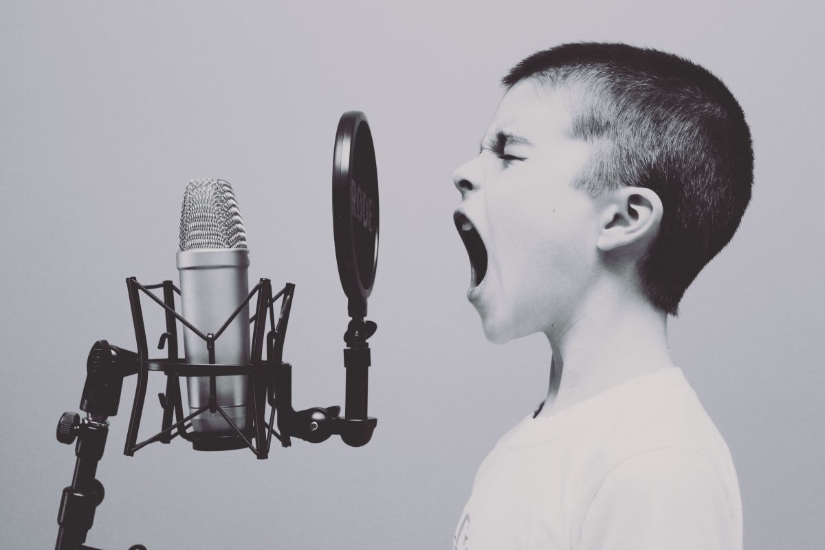 ein kleiner Junge schreit in ein Mikrofon mit Popschutz
