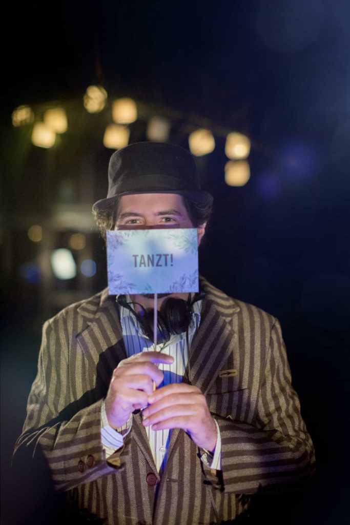 Portrait von Event-DJ Markus Rosenbaum, der ein Schild mit der Aufschrift Tanzt! vor seinem Gesicht hält