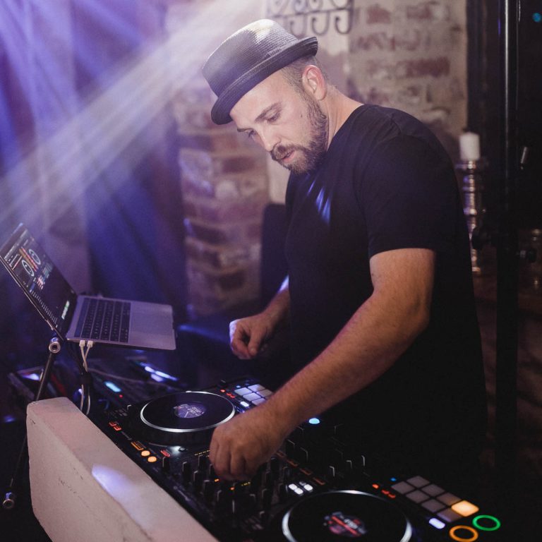 DJ Dominik steht hinter seinem Mischpult und bedient die Regler