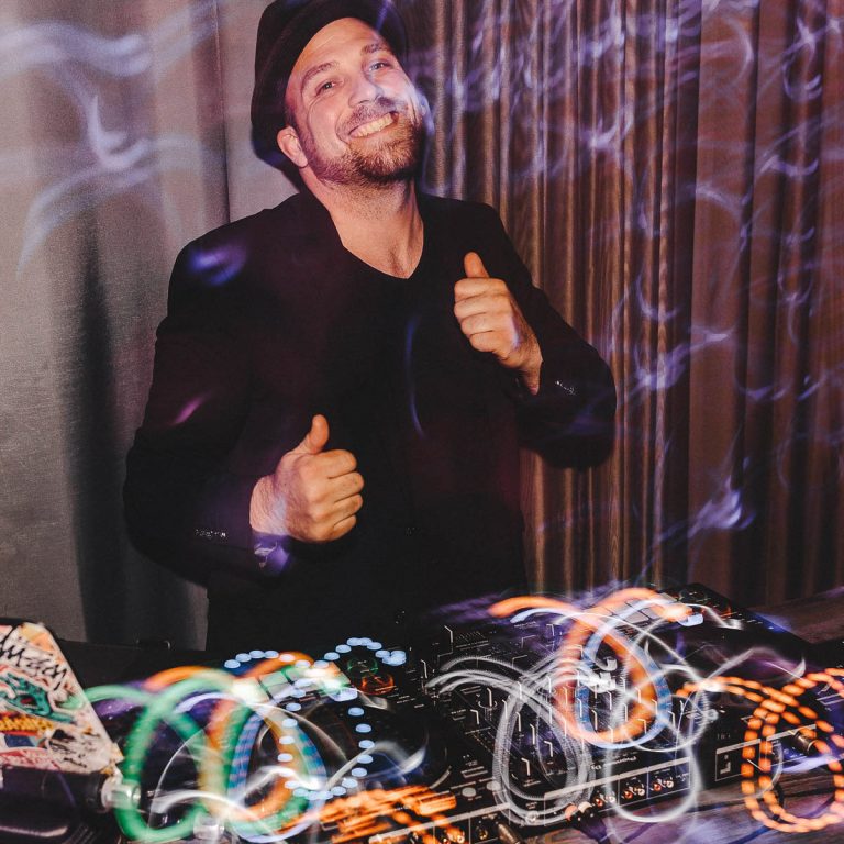 DJ Dominik steht hinter seinem DJ Controller und hebt die Daumen hoch